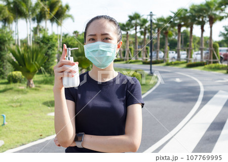 Young woman in medical protective mask and holding an alcohol in hand. campaign to use protective mask and alcohol  for protect COVID19 107769995