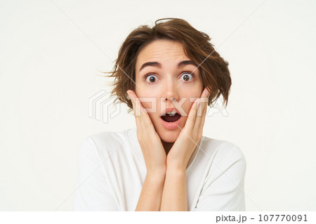 Portrait of girl with surprised face, makes shocked expression, stands over white background Portrait of girl with surprised face, makes shocked expression, stands over white background 107770091