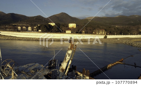 Close-up of old and destroyed ship trunk and gull sitting on a rusty pipe against the sunset sky. Shot. Marine landscapes 107770894