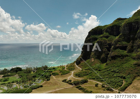 Aerial view of the Oahu coastline with majestic mountains, a winding road, and the Pacific Ocean in Hawaii 107773070
