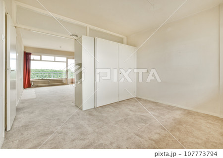 an empty room with white walls and carpeted floor, there is a large mirror on the wall to the right an empty room with white walls and carpeted floor, there is a large mirror on the wall to the right 107773794