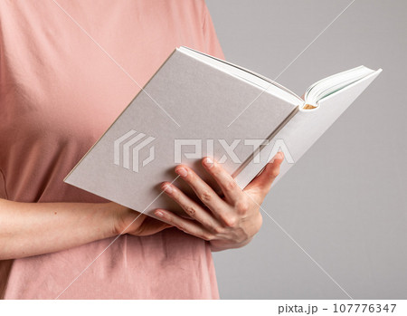 Hand holding open book in hardcover, reading literature Hand holding open book in hardcover, reading literature 107776347