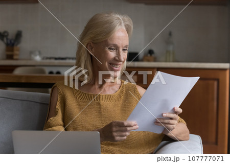 Happy cheerful senior homeowner woman reading paper document 107777071