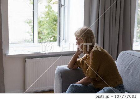 Depressed lonely middle aged woman looking at open window 107777083