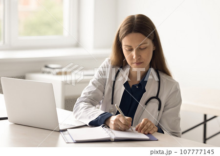 Focused woman therapist makes note in notepad Focused woman therapist makes note in notepad 107777145