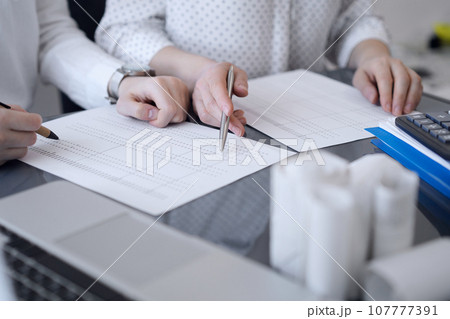 Two accountants use a calculator and laptop computer for counting taxes or revenue balance. Business, audit, and taxes concepts Two accountants use a calculator and laptop computer for counting taxes or revenue balance. Business, audit, and taxes concepts 107777391