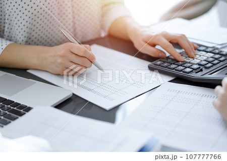 Woman accountant using a calculator and laptop computer while counting taxes with a client or a colleague. Business audit team, finance advisor 107777766