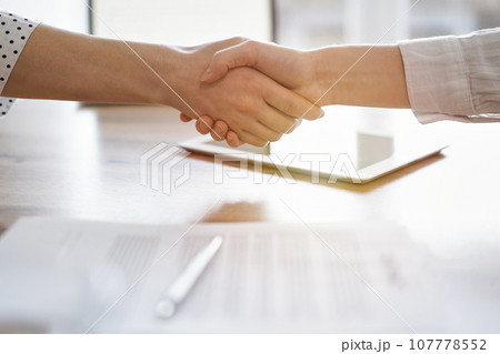 Business people shaking hands above contract papers just signed on the wooden table, close up. Lawyers at work. Partnership, success concept Business people shaking hands above contract papers just signed on the wooden table, close up. Lawyers at work. Partnership, success concept 107778552