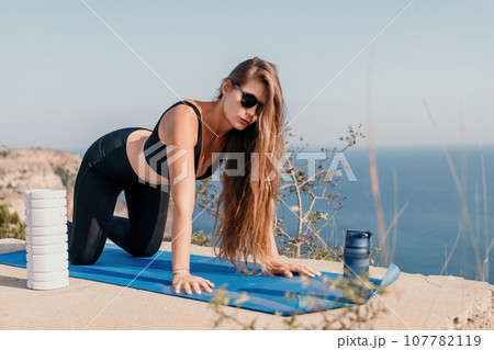 Fitness woman sea. Outdoor workout on yoga mat roller in park near to ocean beach. Female fitness pilates yoga routine concept. Healthy lifestyle. Happy fit woman exercising with rubber band in park. 107782119