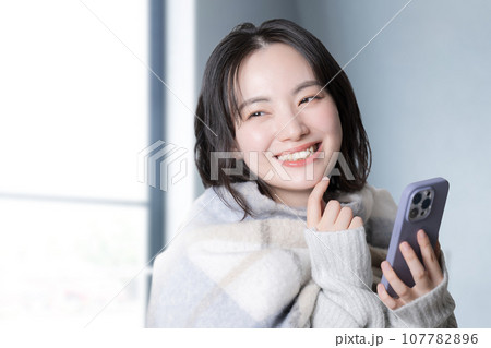 窓際でスマホを操作する若い笑顔の女性の秋冬のイメージ 窓際でスマホを操作する若い笑顔の女性の秋冬のイメージ 107782896