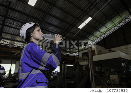 Women engineer drinking water from plastic bottle after working at factory during break. Women engineer drinking water from plastic bottle after working at factory during break. 107782936