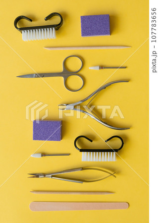Professional manicure tools on yellow background. Manicure set. Top view. Cuticle pusher, cuticle trimmer and purpose scissor. Set of manicure and pedicure tools and cosmetics with space Professional manicure tools on yellow background. Manicure set. Top view. Cuticle pusher, cuticle trimmer and purpose scissor. Set of manicure and pedicure tools and cosmetics with space 107783656
