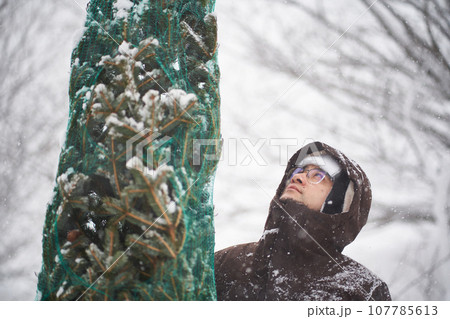 A man brought a Christmas tree into his yard during a snowstorm. 107785613