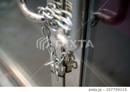 Chain and padlock on closed business glass door with metal handles 107789128