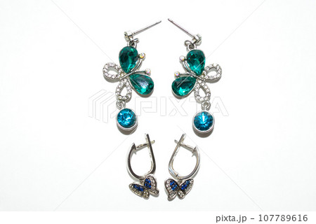 Two pairs of female silver earrings with shiny crystals and butterflies isolated on white background Two pairs of female silver earrings with shiny crystals and butterflies isolated on white background 107789616