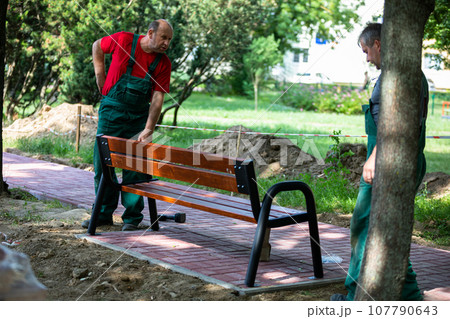 Physical workers set up a park bench at a designated spot in a city park. 107790643