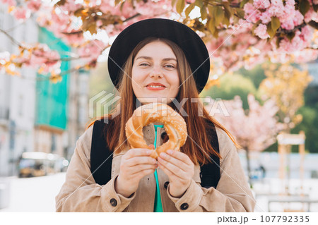 Attractive young female tourist is holding pretzel, traditional polish or turkish bagel. Traveling Europe in spring. High quality photo Attractive young female tourist is holding pretzel, traditional polish or turkish bagel. Traveling Europe in spring. High quality photo 107792335