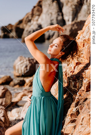 Woman green dress sea. Woman in a long mint dress posing on a beach with rocks on sunny day. Girl on the nature on blue sky background. Woman green dress sea. Woman in a long mint dress posing on a beach with rocks on sunny day. Girl on the nature on blue sky background. 107793470