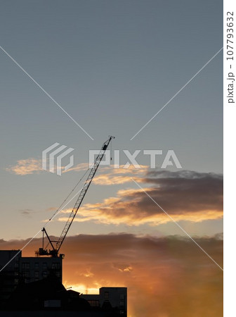 Construction crane silhouette against city skyline at sunset.Bright orange sunset. 107793632