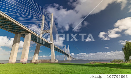 Vasco da Gama bridge timelapse hyperlapse with green lawn on a waterfront and blue cloudy sky. Lisbon, Portugal. Vasco da Gama bridge timelapse hyperlapse with green lawn on a waterfront and blue cloudy sky. Lisbon, Portugal. 107793868