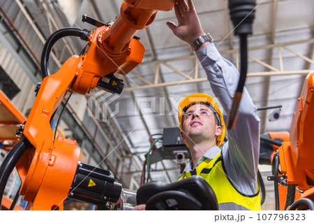 Smart modern engineer male using modern robot technology. Robotic welding arm setup in automation production process in factory Smart modern engineer male using modern robot technology. Robotic welding arm setup in automation production process in factory 107796323