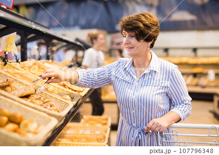 Mature woman examines bakery products in the grocery section of the supermarket 107796348