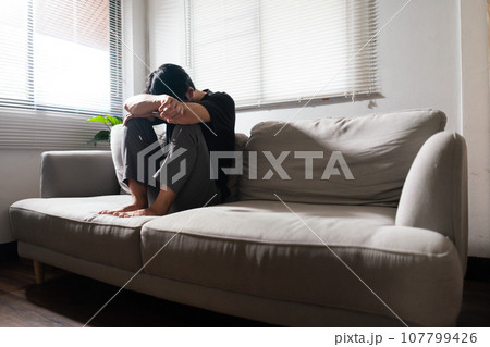 Man with mental health problem sitting on couch to resting head on his arms with depressed emotion 107799426