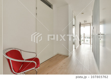 an empty room with a red chair on the floor and a white door in the hallway leading to another room 107803762