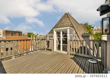 a roof on a house with wood sidings and white trim around the windows, looking out onto the street 107803811