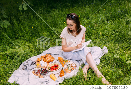 Beautiful woman on picnic. She smiles, eats strawberries and enjoys summer. 107805180