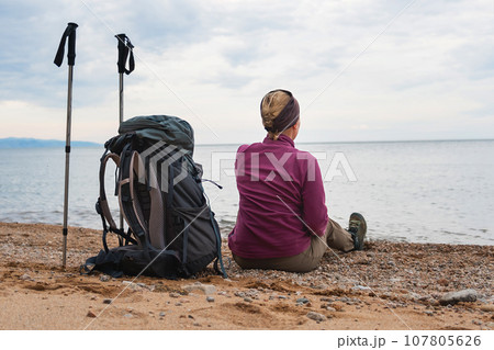 Hiking tourism adventure. Backpacker woman resting after hiking looking at beautiful view. Hiker girl lady tourist with backpack sitting near lake. Hiker woman enjoy hike tourism active vacation Hiking tourism adventure. Backpacker woman resting after hiking looking at beautiful view. Hiker girl lady tourist with backpack sitting near lake. Hiker woman enjoy hike tourism active vacation 107805626