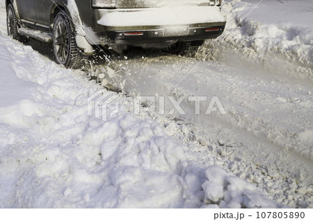 Road snow flies up from a vehicle's spinning wheel. Car's wheels spin and spew up pieces of snow it attempts to gain traction on the slippery road. Road snow flies up from a vehicle's spinning wheel. Car's wheels spin and spew up pieces of snow it attempts to gain traction on the slippery road. 107805890