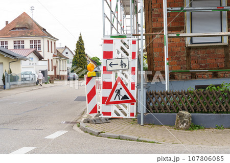 On the enclosing structure there is a warning sign for road works and the direction of pedestrian movement. 107806085