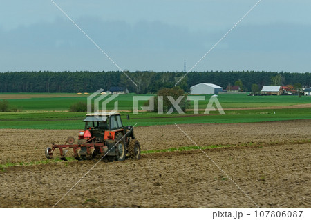 A tractor with plows stands near a plowed field. 107806087