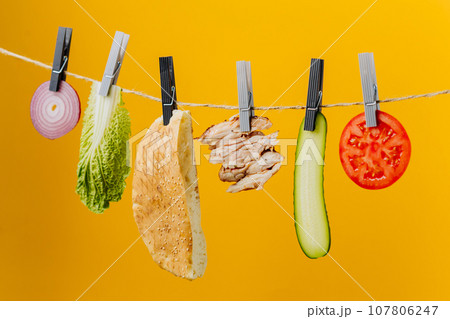 Doner kebab with ingredients hanging on a thread in the air : beef meat, lettuce, onion, tomatoes, cheese, cucumber. Yellow background 107806247