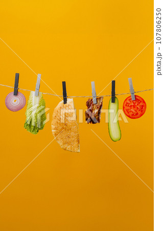 Doner kebab with ingredients hanging on a thread in the air : beef meat, lettuce, onion, tomatoes, cheese, cucumber. Yellow background 107806250