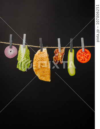 Doner kebab with ingredients hanging on a thread in the air : beef meat, lettuce, onion, tomatoes, cheese, cucumber. Black background 107806251