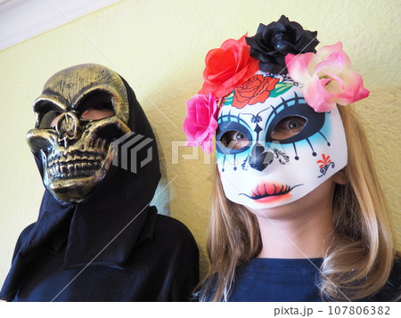 Children dressed in black costumes and scary Halloween masks. Girl in a Mexican Kalaka Calavera mask. A boy wearing a horrible skull mask with a black hood. All Hallows Eve or All Saints Eve theme Children dressed in black costumes and scary Halloween masks. Girl in a Mexican Kalaka Calavera mask. A boy wearing a horrible skull mask with a black hood. All Hallows Eve or All Saints Eve theme 107806382