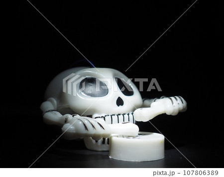 Skull with drumsticks and drum. Terrible clockwork toy. The skeleton is made of the skull, bones, hands and fingers. Black background. Halloween and horror theme. White skull with black eye sockets. Skull with drumsticks and drum. Terrible clockwork toy. The skeleton is made of the skull, bones, hands and fingers. Black background. Halloween and horror theme. White skull with black eye sockets. 107806389