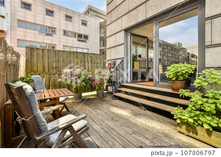 a wooden deck with chairs and potted plants in the foreground, on a sunny day at an apartment building 107806797