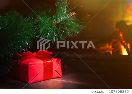 Christmas composition, gift under the tree near a burning fireplace, close-up Christmas composition, gift under the tree near a burning fireplace, close-up 107806889