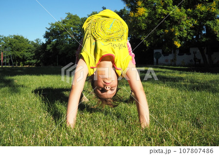 Caucasian girl 8 years old doing a bridge exercise on the grass in the park. Playground. Children's sports. Spine health, treatment of scoliosis 107807486