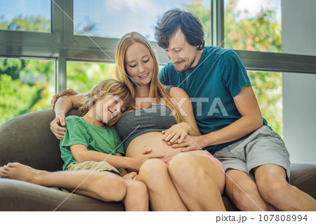Expectant parents, mom, dad, and their eldest son share a heartwarming moment on the sofa, discussing the exciting journey of pregnancy 107808994