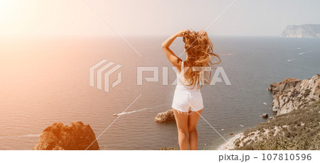 Woman summer travel sea. Happy tourist enjoy taking picture outdoors for memories. Woman traveler posing over sea bay surrounded by volcanic mountains, sharing travel adventure journey 107810596
