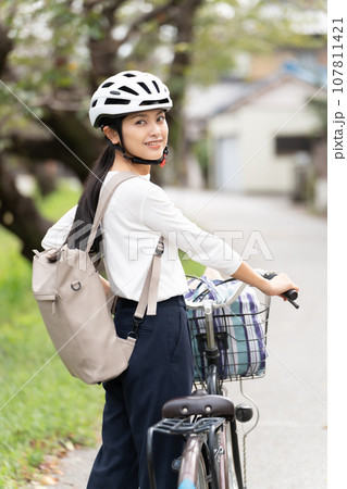 サイクリングヘルメットをかぶって自転車を引いて歩く若い女性 107811421