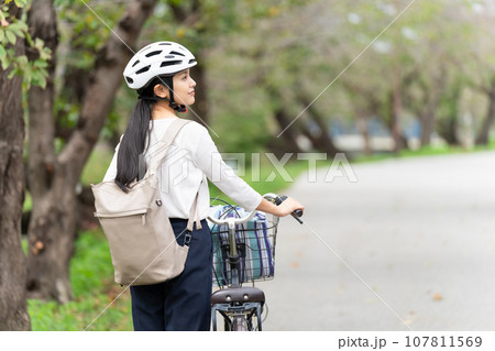 サイクリングヘルメットをかぶって自転車を引いて歩く若い女性 107811569