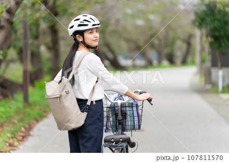 サイクリングヘルメットをかぶって自転車を引いて歩く若い女性 107811570
