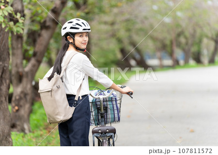 サイクリングヘルメットをかぶって自転車を引いて歩く若い女性 107811572