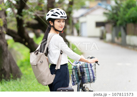 サイクリングヘルメットをかぶって自転車を引いて歩く若い女性 サイクリングヘルメットをかぶって自転車を引いて歩く若い女性 107811573
