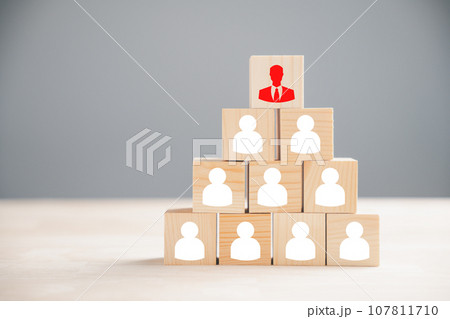 Red manager icon visually distinct from collection of staff employee icons printed on wooden block. Illustrates the importance of talent, leadership, development of individuals within business context 107811710